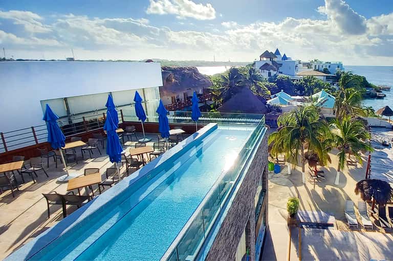 Infinity pool overlooking calm bay waters with blue umbrellas and waterfront buildings