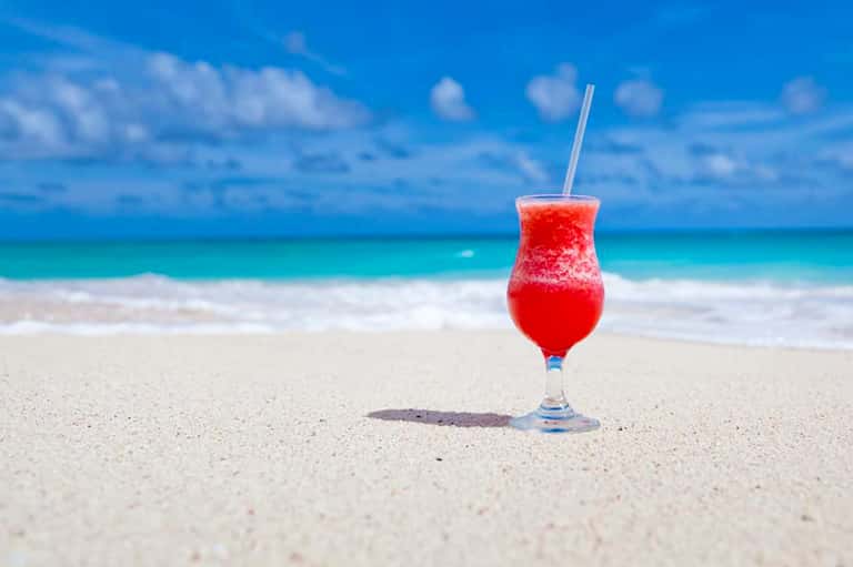 Red tropical cocktail on white sand beach with crystal ocean water and blue sky
