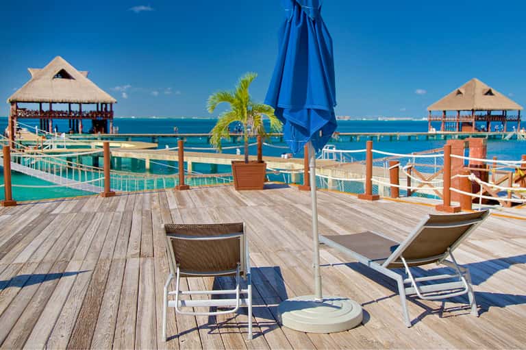 Waterfront deck with thatched cabanas, lounge chairs, and turquoise water views