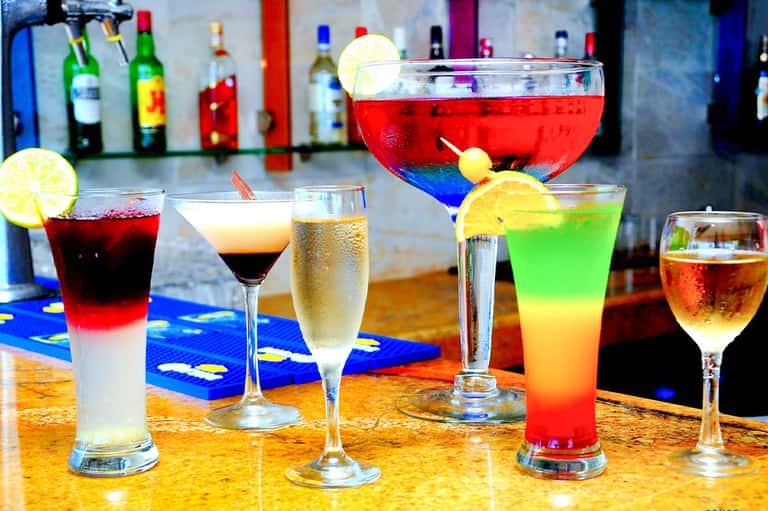 Colorful tropical cocktails on bar counter with bottles in background