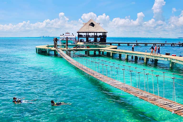 Tropical pier with wooden walkway, thatched-roof pavilion, and crystal turquoise water for snorkeling