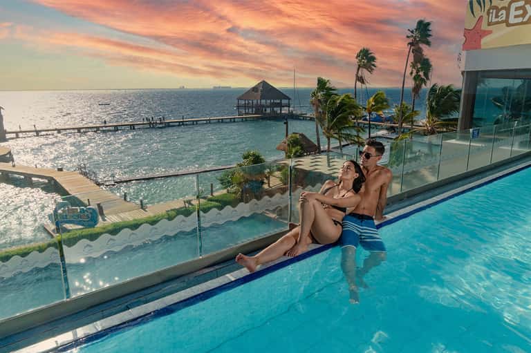 Couple relaxing in infinity pool at sunset with ocean view, beach resort, and palm trees