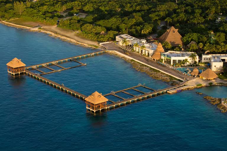 Aerial view of waterfront resort with dock, thatched structures, and tropical vegetation