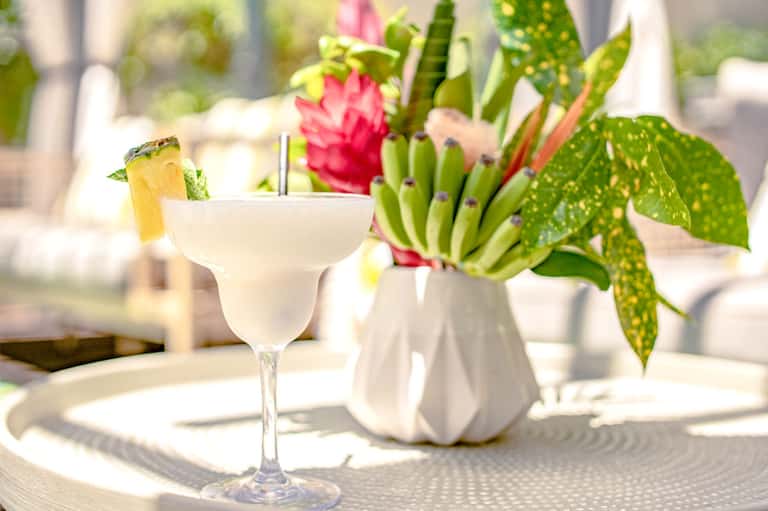 Tropical cocktail with pineapple garnish and pink flower arrangement on table