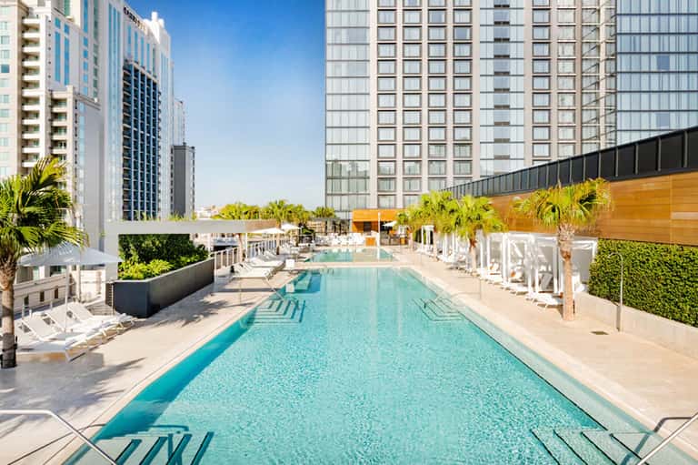 Lap pool at urban resort surrounded by high-rise buildings with white loungers and palm trees