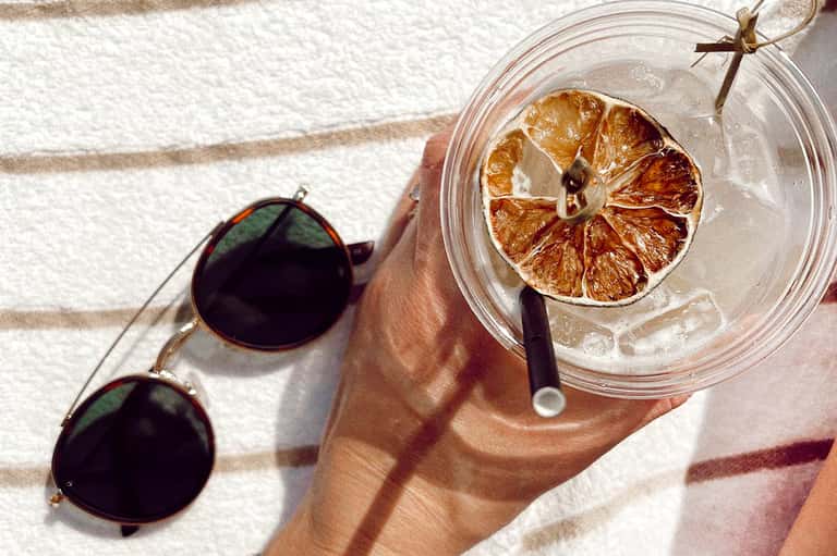 Overhead view of sunglasses and iced drink with dried lemon slice on towel