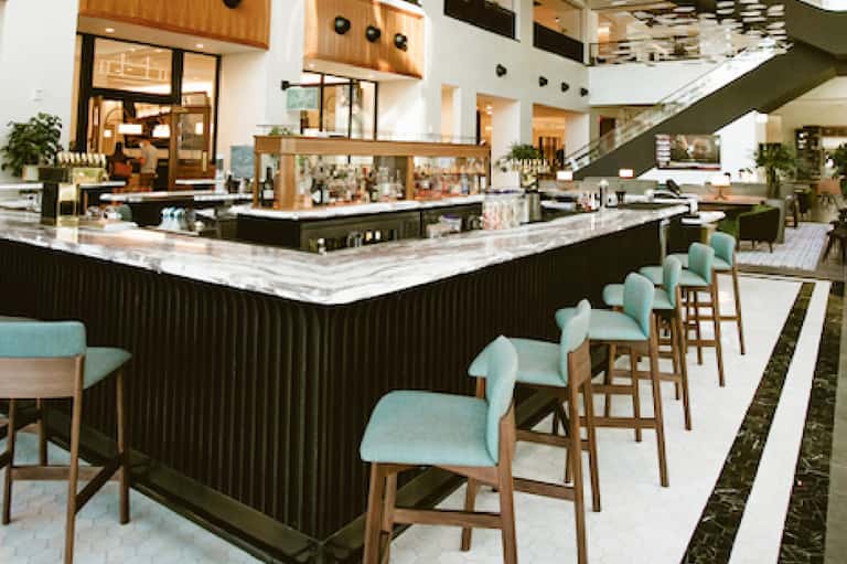 Modern hotel lobby bar area with turquoise bar stools, marble counters, wooden accents, and contemporary design