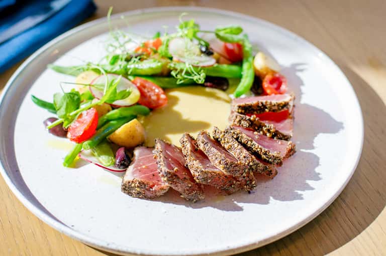 Artfully plated gourmet meal with seared meat, vegetables, and sauce on white plate