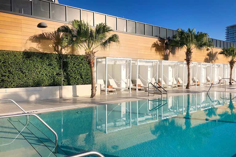 Contemporary pool deck with glass-enclosed lounge area and palm trees against modern building