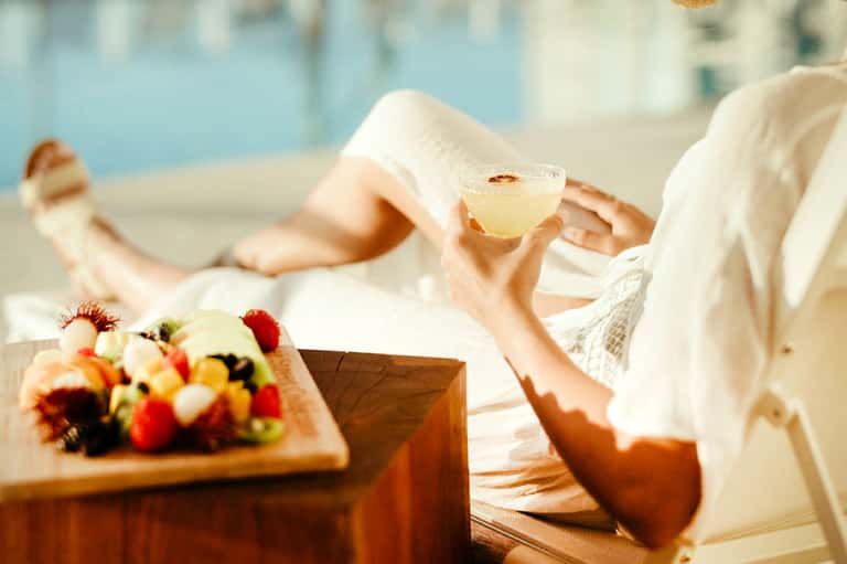 Guest enjoying tropical drink poolside with fresh fruit appetizer and ocean view in background