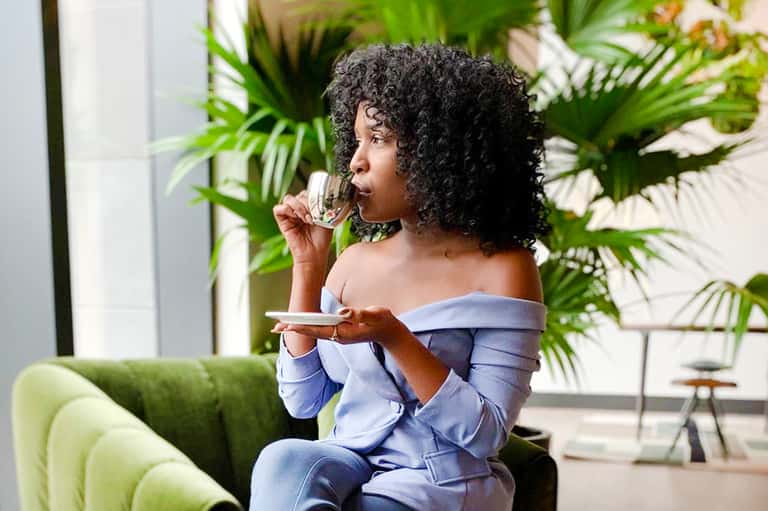 Woman in blue off-shoulder top eating while seated on green chair with tropical plants in background