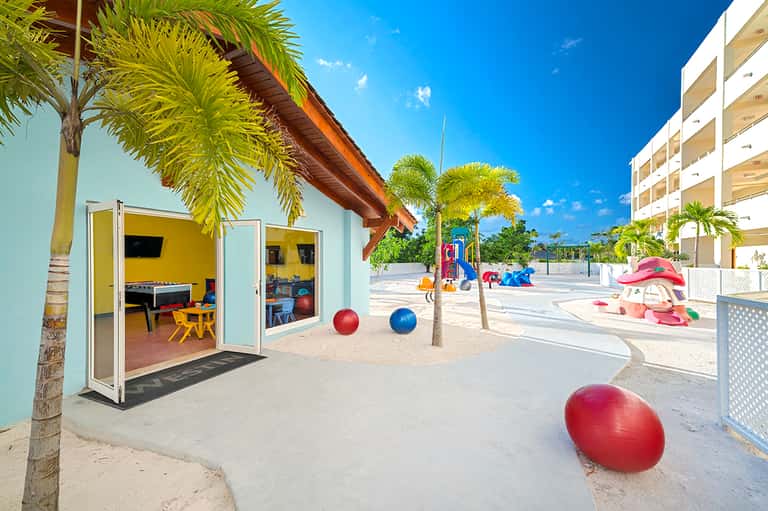 Beach kids club with colorful play structures, palm trees, and bright modern facility by ocean