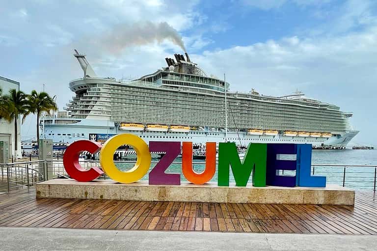 Colorful 'COZUMEL' sign on wooden dock with large cruise ship docked in harbor background