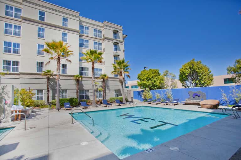 Resort pool surrounded by palm trees with multi-story hotel building and clear blue sky