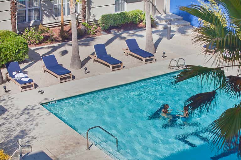 Resort pool area with blue loungers under palm trees, guests swimming in turquoise water