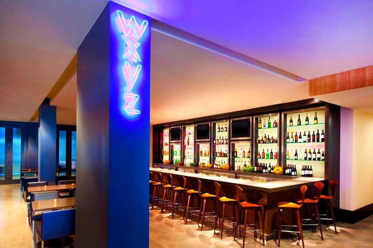 Modern lounge bar with neon signage, illuminated liquor shelves, and ambient purple lighting