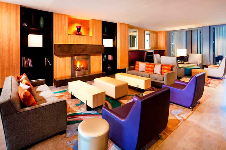 Contemporary lounge with orange wood paneling, fireplace, colorful furniture, and modern art