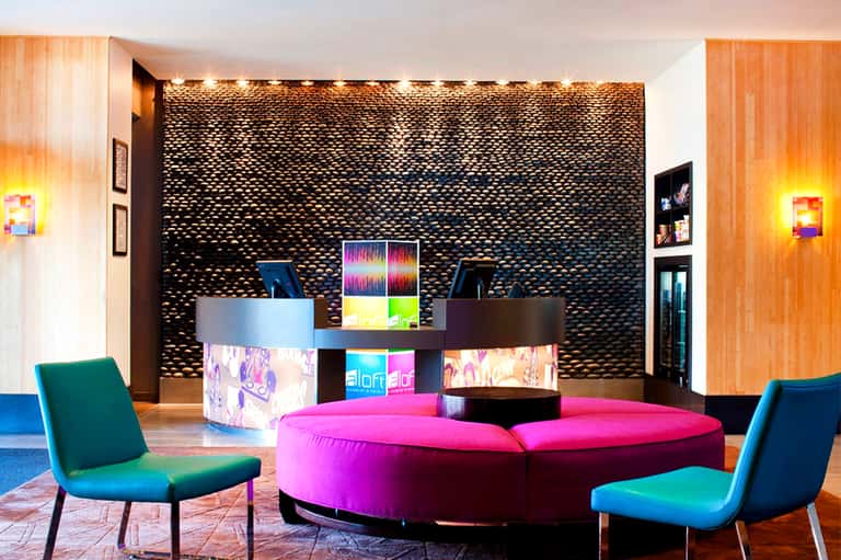 Modern hotel lobby interior with magenta circular seating, textured black wall, colorful accent lighting