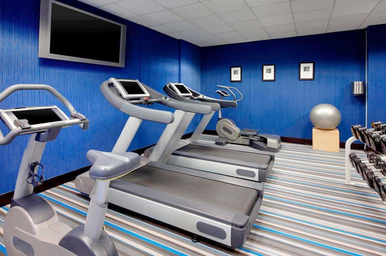 Modern fitness center with blue walls, treadmills, stationary bikes, exercise equipment and flat-screen monitor