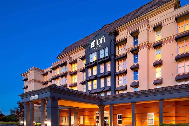 Aloft Hotel exterior at dusk with pink and blue architecture, illuminated entrance, and clear sky