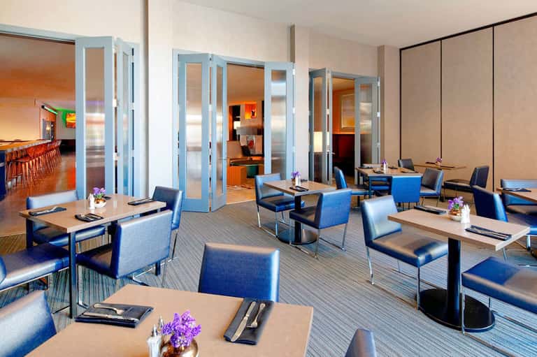 Modern hotel restaurant with blue chairs, wooden tables, and glass partition doors