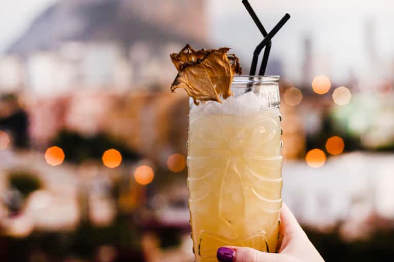 Craft cocktail with dried fruit garnish and black straw in tall glass with blurred background