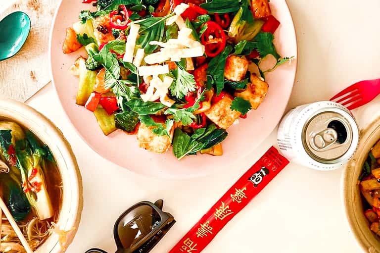 Overhead view of colorful Asian cuisine on pink plate with fresh herbs and vegetable garnish