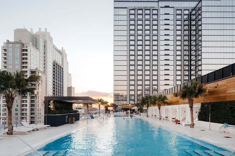 Modern hotel pool deck between tall buildings at sunset with lounging chairs