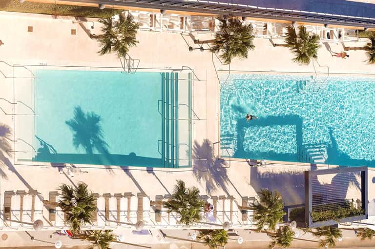 Aerial view of two rectangular pools with palm trees and white deck chairs