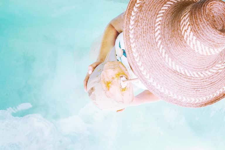 Person in turquoise pool wearing pink straw hat and white swimwear
