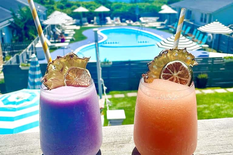 Two decorative cocktails with pineapple garnish overlooking resort pool and umbrellas