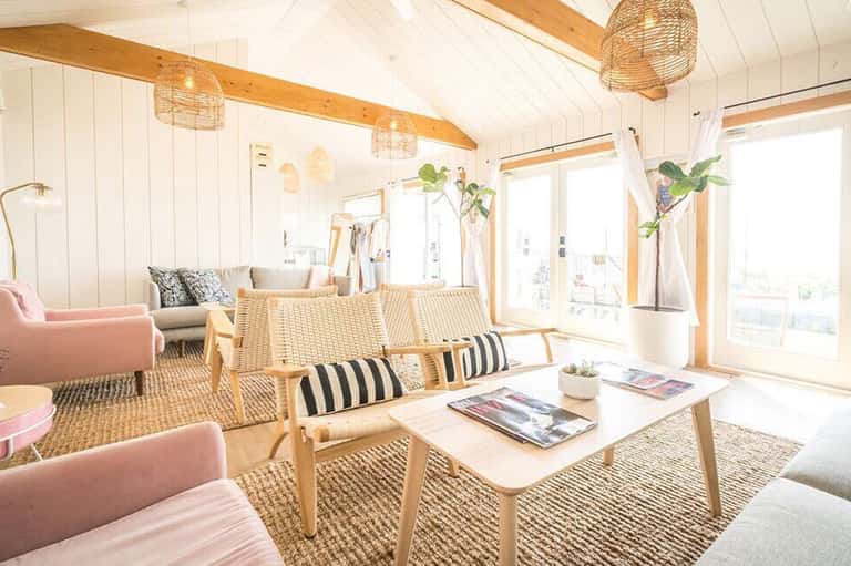 Bright, modern lounge with wooden beams, wicker pendant lights, pink seating, and natural sunlight