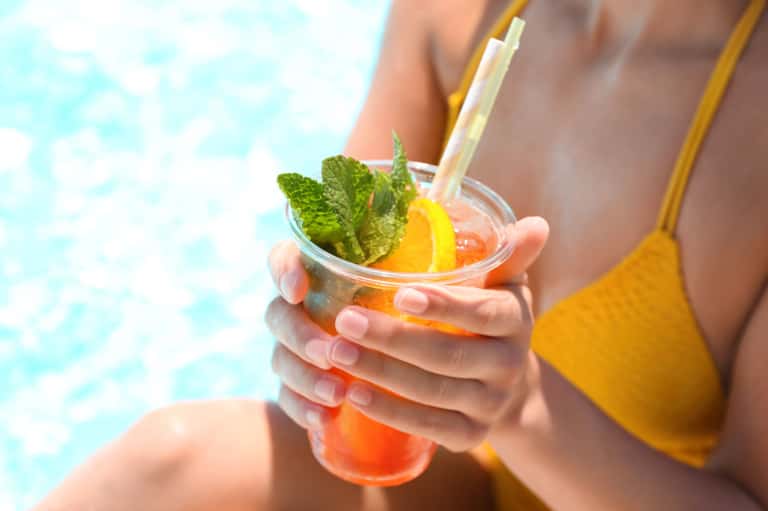 Guest holding tropical cocktail by pool with mint garnish and colorful drink