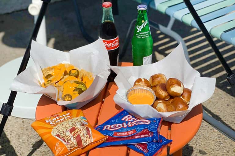 Poolside snacks including tacos, beverages, popcorn, and pretzel bread on chair