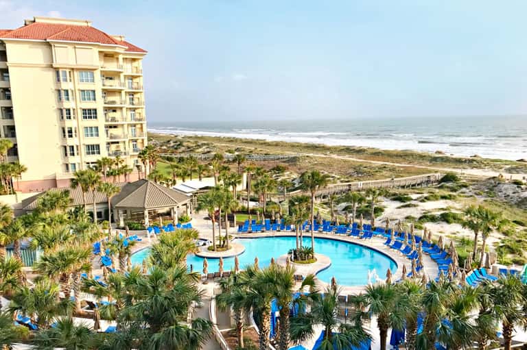 Beachfront resort with cream-colored building, curved pool with blue lounge chairs, and ocean view