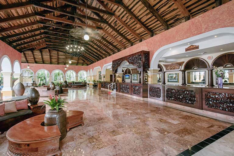 Grand pink colonial-style hotel lobby with arched doorways, wooden ceiling beams, ornate details, and marble floors.
