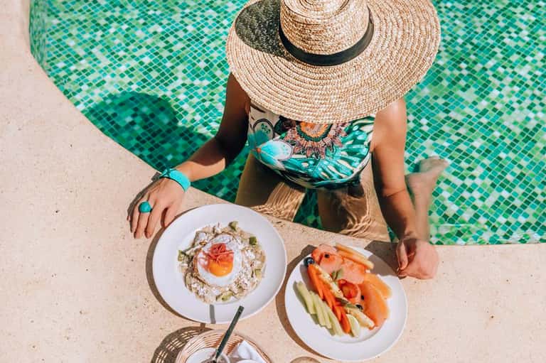 Woman in straw hat poolside enjoying plates of fresh seafood and vegetables