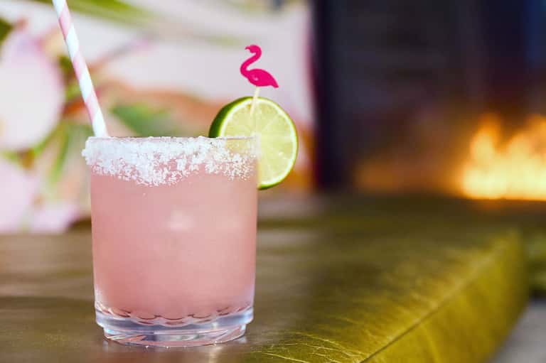 Pink margarita with salt rim and lime wheel garnish on a bar counter