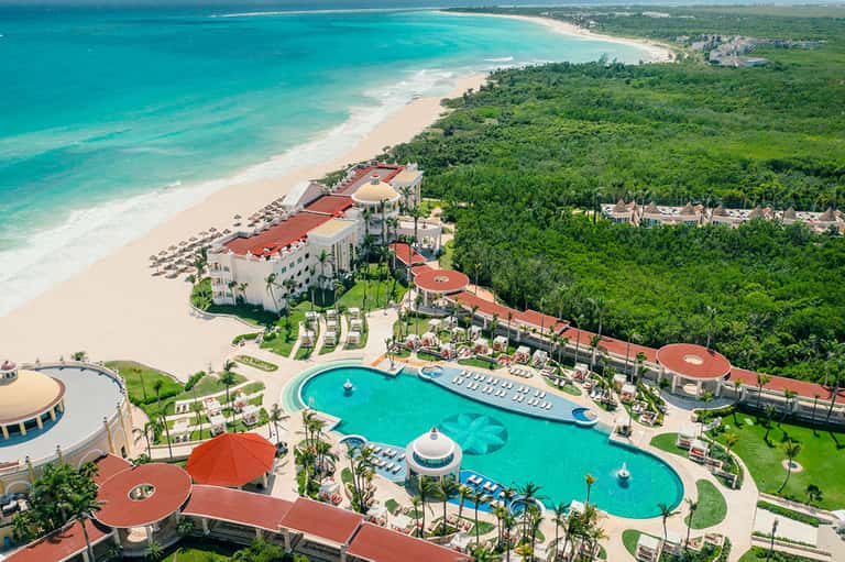 Aerial view of beachfront resort with turquoise pools, red roofs, pristine beach, and tropical grounds