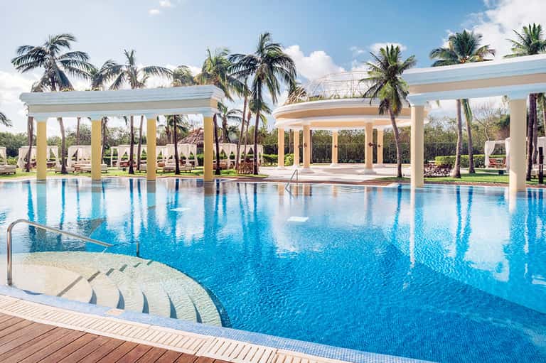 Elegant resort swimming pool with covered pergola, palm trees, and lounge seating