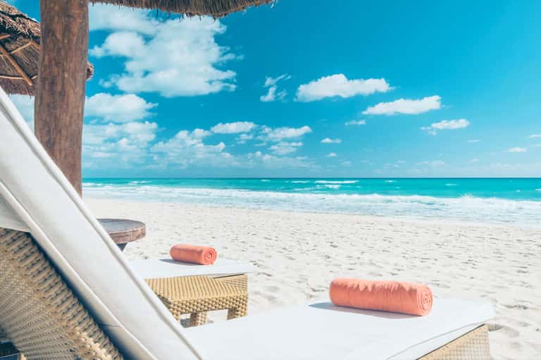 Beachfront cabana with thatched roof, ocean view, lounge chairs, and rolled coral towels