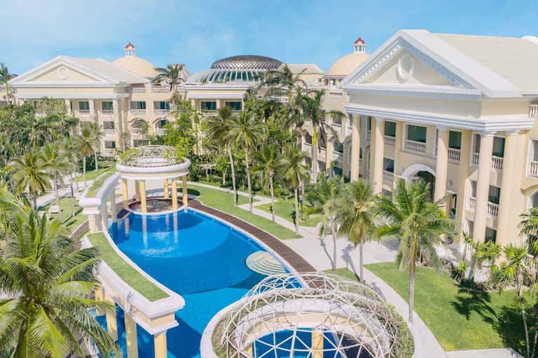 Luxurious resort courtyard with pale yellow neoclassical buildings and blue pools