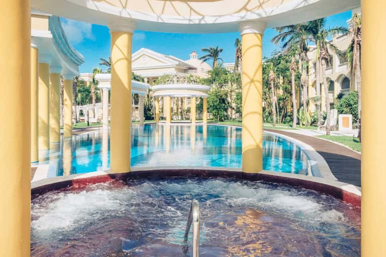 Indoor spa pool surrounded by yellow columns, elegant architecture, and palm-lined grounds