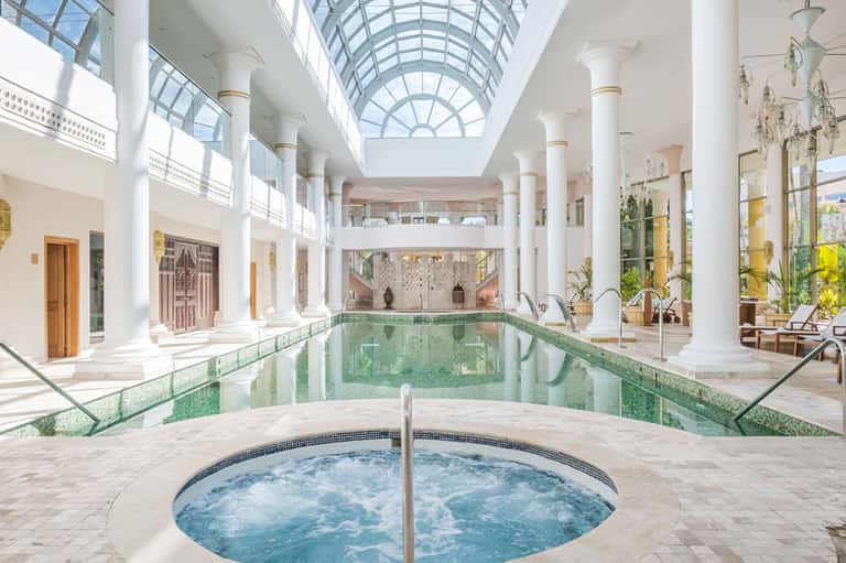 Indoor spa area with large heated jacuzzi tub and lap pool beneath glass skylight ceiling