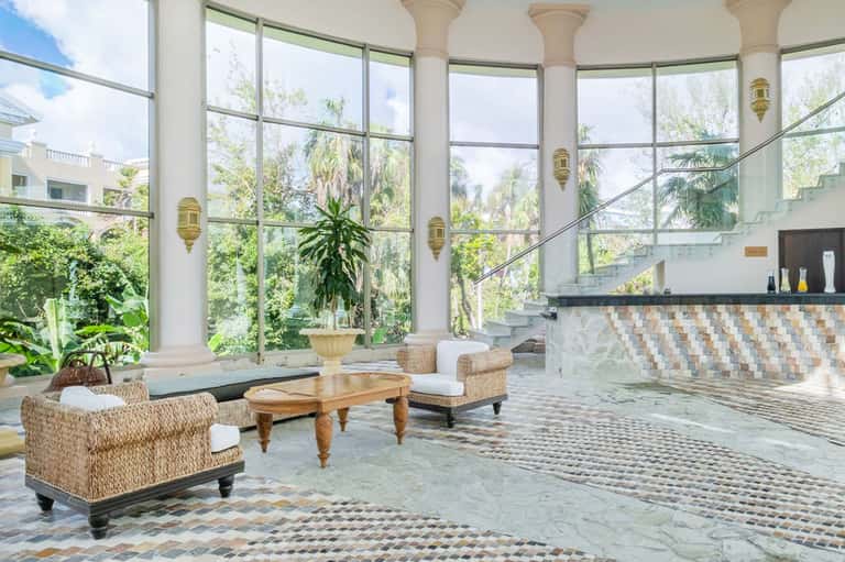 Luxury spa interior with floor-to-ceiling windows, marble floors, woven chairs, and hanging lamps