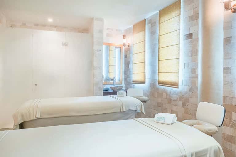 Minimalist spa treatment room with two massage beds and natural stone tile walls with warm lighting