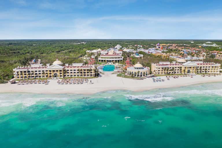 Aerial view of colorful beachfront resort complex with pools, beach, and surrounding landscape