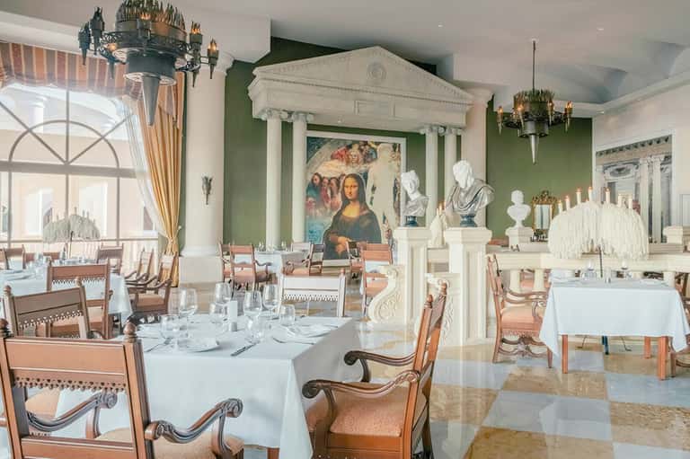 Upscale dining room with neoclassical design, green walls, and fine place settings