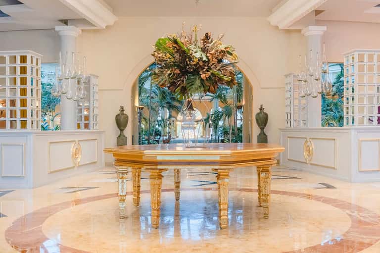 Elegant grand ballroom with golden piano, marble floors, and tropical archway decoration