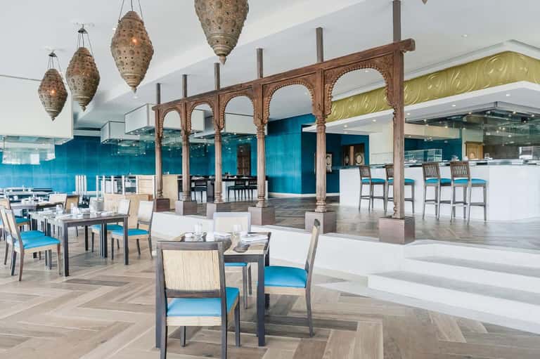 Modern restaurant with carved wooden archway, turquoise backsplash, bar seating, and decorative lanterns